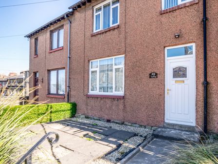 A terraced house with brown pebble dash walls white door and windows and small garden area at Tomeg in Amble-by-the-Sea