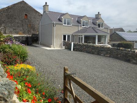 A stone house with three dormer windows a gravel driveway and a garden with flowers at Ty Top in Llanfaethlu