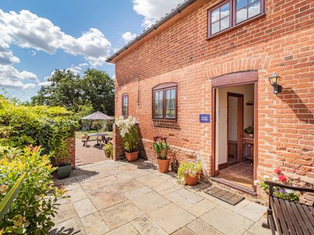 An outdoor patio area with potted plants and a brick building with windows and an open door at Punch Cottage in Little Glemham near Wickham Market
