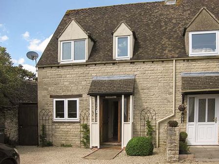 An exterior view of a stone cottage with windows and a small porch with open doors at Hour Cottage in Stow-on-the-Wold