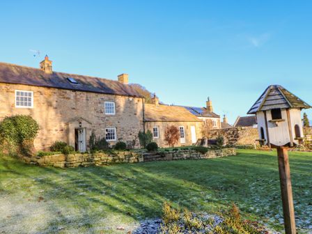 A stone house with a garden and birdhouse on a post at East Farm House in Humshaugh near Hexham