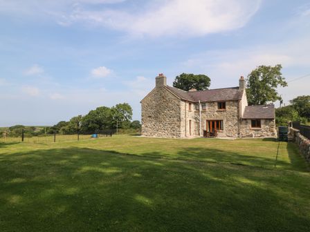 A stone farmhouse with a large lawn and trees in the background at Y Berth Ddu Farmhouse in Clynnog Fawr
