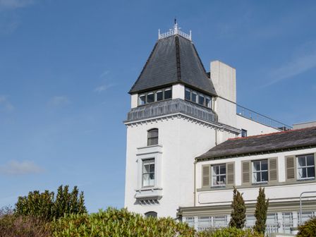 A white building with a tower and windows surrounded by bushes at The Moorings in Deganwy near Llandudno