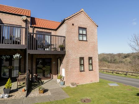 A brick two-story house with a balcony and patio doors overlooking a grassy area at Sunnybrae in Whitby