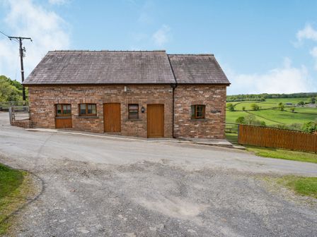 A brick building with wooden doors and windows next to a road and green fields at Bwthyn-y-Rhiw in Penybanc near Llandeilo