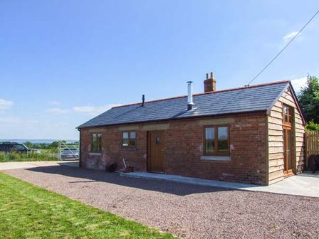 A single story brick house with a gravel driveway and grass lawn at Dovetail in Westbury-on-Severn