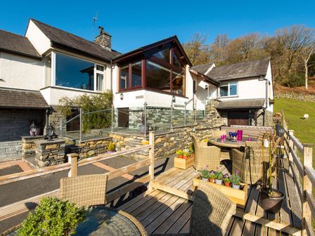An outdoor patio area with wicker chairs and tables outside a white house with stone detailing at Browside Little Arrow near Coniston
