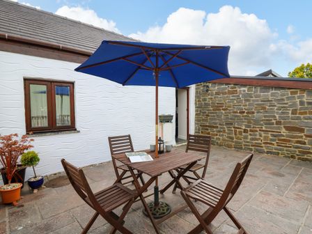 An outdoor patio with wooden table and chairs under a blue umbrella and potted plants at Yr Hen Ysgubor Trelech near St Clears