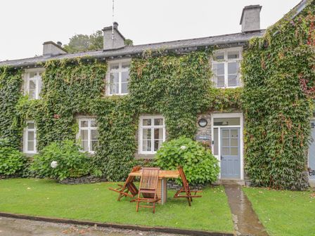 A stone cottage covered with ivy with wooden garden chairs and table on the lawn at Bibby Lot in Graythwaite near Hawkshead