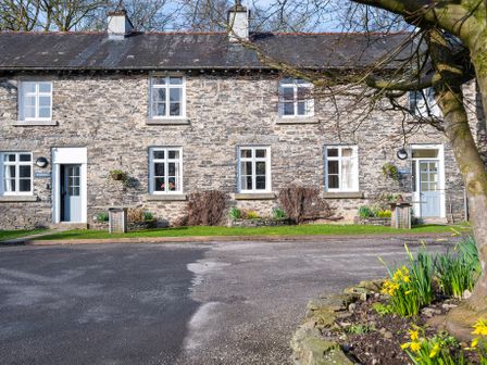 A stone building with multiple windows and doors with a paved driveway and flower garden at Greenhowes Graythwaite near Hawkshead