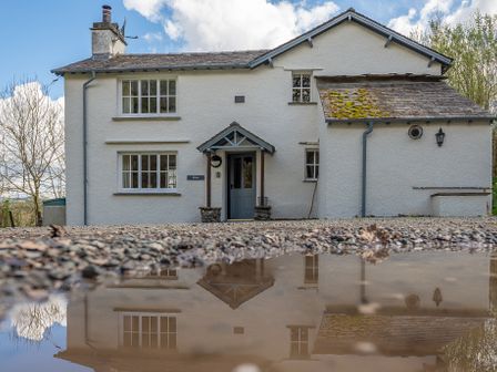 Front view of a white two story house with windows a door and a small porch reflected in a puddle at Hilltop in Graythwaite near Hawkshead
