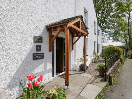 White exterior of a building with a wooden porch over the entrance and potted plants near the door at Fox Barn in Staveley