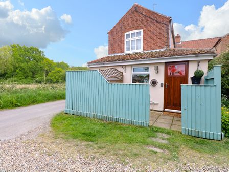 A brick house with a wooden door and blue fence beside a country road at 2 Lock Cottages Honing near East Ruston