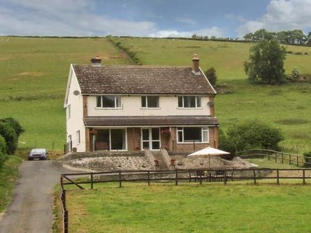 A detached house with a paved driveway and outdoor seating area with umbrella in a rural area at Cwmgilla Farm in Knighton