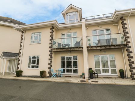 The exterior of a two story beige building with balconies and patio furniture at Tywod a Mor in Morfa Nefyn