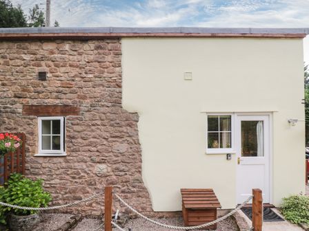 A building exterior with a stone wall on the left and a cream painted wall with a white door and window on the right at Woods Edge in Mitcheldean