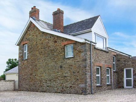 A stone house with multiple windows and chimneys on a gravel driveway at The Grange in Little Haven near Haverfordwest