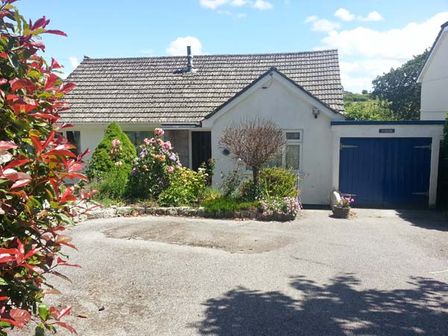 A single-story house with a tiled roof a garden with bushes flowers and a tree a driveway and a blue garage door at Joylands in Falmouth