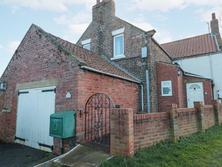 A brick house with a white door and a green utility box near a metal gate at Airy Hill Old Farmhouse Whitby