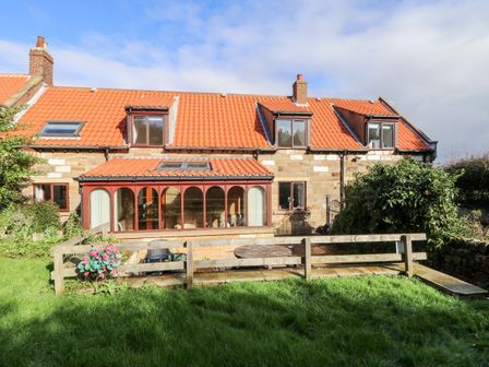 A stone house with red tiled roof and a glass conservatory overlooking a garden with grass and wooden fence at Airy Hill Farm Cottage in Whitby
