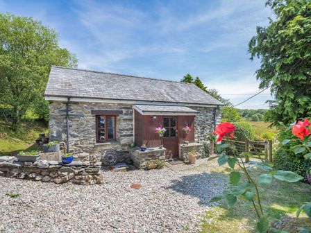 A stone cottage with a gravel yard flowers and plants near a gate at Bwythyn Y Wennol in Nantmor near Beddgelert