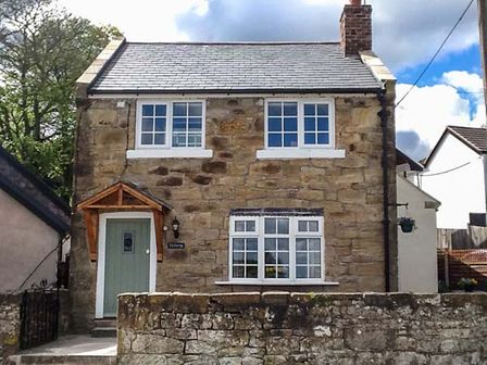 A stone house with a green door and white framed windows behind a stone wall