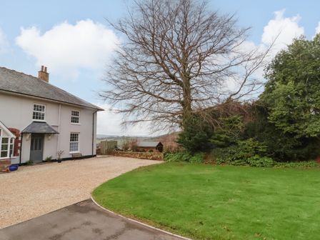 A gravel driveway next to a white house with a garden and trees at The Well House Apartment in Watchet