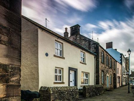 A row of stone and plaster houses along a sidewalk with a streetlamp in a town