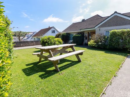 A garden with a wooden picnic table and a house with bushes at Summerfield Cottage in Gorran Haven