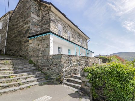 A stone building with white and blue trim next to stone steps and greenery at Goronwy Cottage in Barmouth