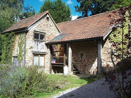 A stone house with a tiled roof and an entrance with wooden pillars surrounded by greenery at The Mill in Bicknoller