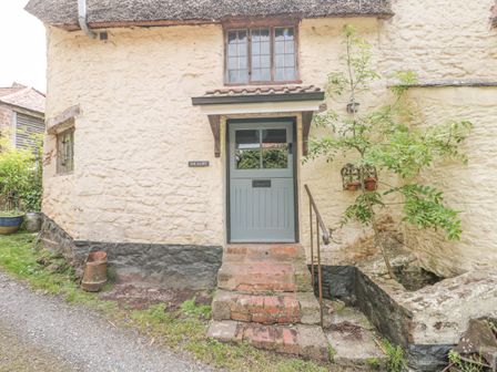 Exterior of a stone cottage with a blue door and brick steps at The Dairy in Bicknoller