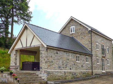 A stone house with multiple windows and an open covered area with a bench and plants at The Old Mill in Dolau near Llandrindod Wells