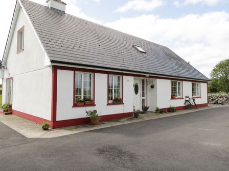 A white house with red trim and a gray roof with flower pots near the windows and a bicycle near the entrance at Lough Mask Road Fishing Lodge in Ballinrobe County Mayo