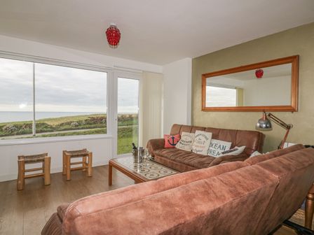 A living room with brown sofas a large window showing a grass field and sea at Spindrift in Porth near Newquay