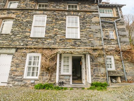 A stone building with white framed windows and an open door with plants at the entrance at The Old Laundry in Clappersgate near Ambleside