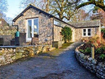 A stone cottage with an outdoor seating area and a gravel driveway at The Potting Shed in Burton-in-Kendal near Kirkby Lonsdale