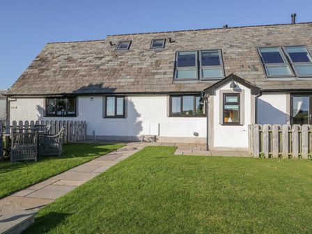 An exterior view of a house with a tiled roof a lawn a stone pathway and outdoor furniture at Bluebell Cottage in Aldingham