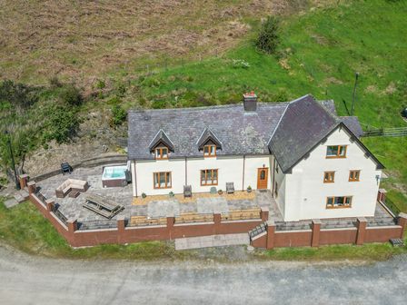 A house with fenced patio area including outdoor seating and a hot tub surrounded by grass and hills at Maesgwyn in Beguildy