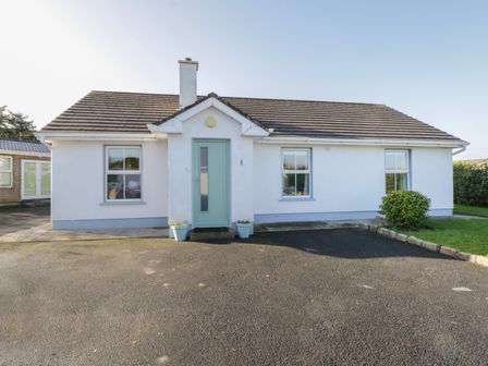 A white single-story house with a green front door two windows and a chimney at Teach Teolai in Carraroe County Galway