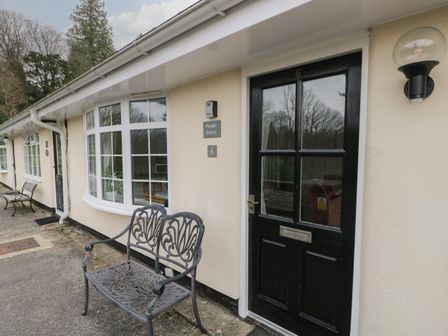 The exterior of a beige building with black doors windows and decorative metal benches at Priory Ghyll in Windermere