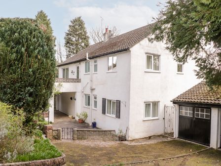 A two-story white house with a small balcony and attached garage surrounded by trees and plants at Treetops in Rhos-On-Sea