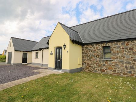 The exterior of a house with a stone and yellow facade a black front door a lawn and a driveway at Tlws Bach Roch near Haverfordwest