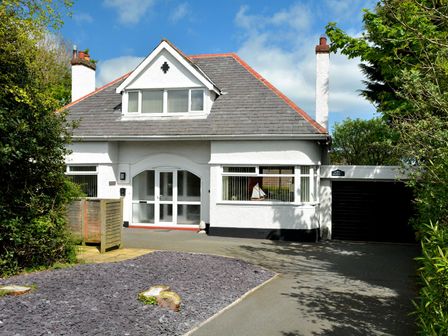 A white house with a grey roof a driveway and a small garden area at Monarfon in Benllech near Red Wharf Bay