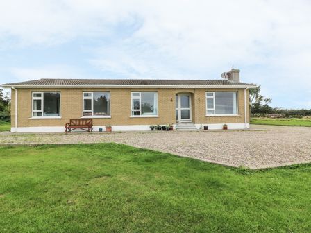 A single-story brick house with five windows and a door with steps in front and gravel driveway with grass in foreground at Findale Carne near Rosslare County Wexford