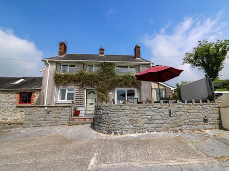 A two-story house with a stone wall a red patio umbrella and a driveway at Aberdauddwr in Lampeter