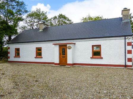 A single-story white cottage with a grey roof three windows and a wooden door at Ferrys in Portsalon County Donegal