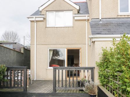 A back view of a two-story house with a wooden deck and railing with potted plants near the entrance at Bryn Y Don Cottage in Benllech