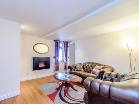 A living room with leather sofas a wooden coffee table a wall-mounted electric fireplace and patterned curtains at Mermaid Cottage in Whitby
