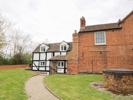 A house with a black and white timber frame and a brick extension with a gravel path and a brick well in the yard at Rose Cottage in Upton upon Severn